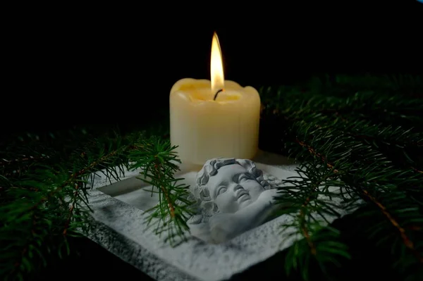 Guardian angel, Fir branches with a burning candle on black background. Christmas tree branches and an Angel lying on the table against darkness. Condolence card concept in christmas time or New year.