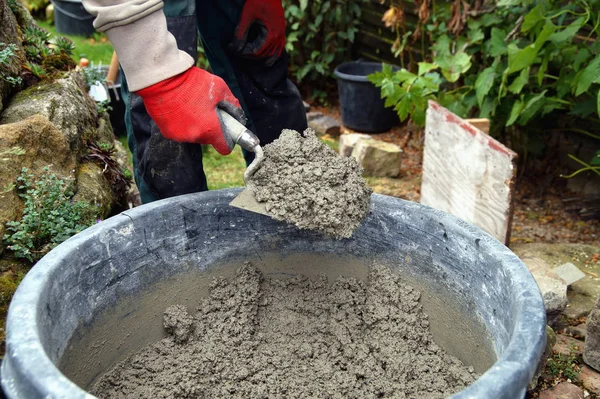 Foundation and form work. Male Worker gloved hands shovels a wet mix of concrete with trowel or putty knife in a bucket at a construction site