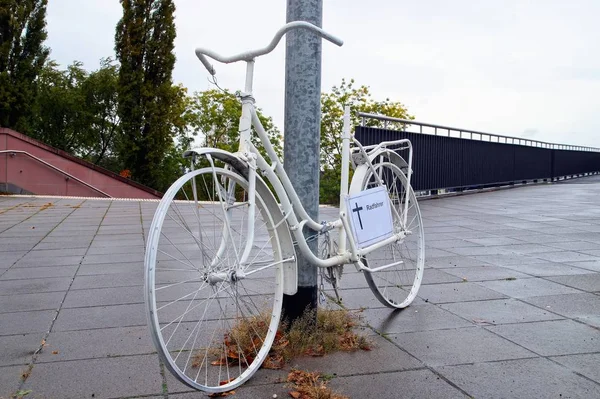 A ghost bike memorial with a german sign - Radfahrer - and a cross for a killed cyclist at Frankfurt Main, Germany streets on a rainy Dreary Day. White ghost bicycle, memorial to a cyclist who died in traffic accident