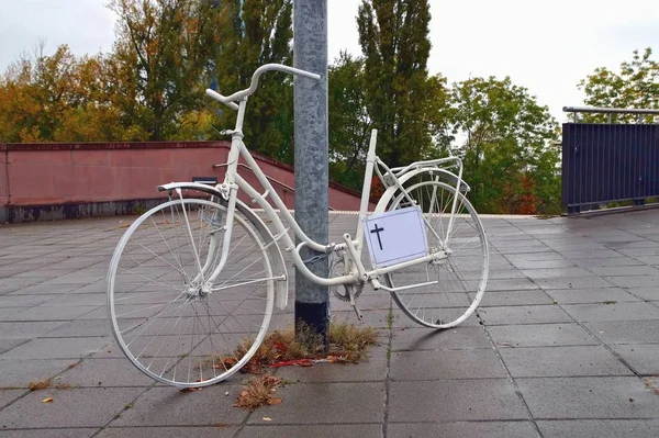 A ghost bike memorial with a cross sign for a killed cyclist at Frankfurt Main, Germany streets on a rainy Dreary Day. White ghost bicycle, memorial to a cyclist who died in traffic accident