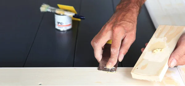 Putty knife in man's hand. DIY worker applying filler to the wood. Removing holes from a wood surface. Preparation of wood before impregnation with varnish. woodwork. Application of putty.