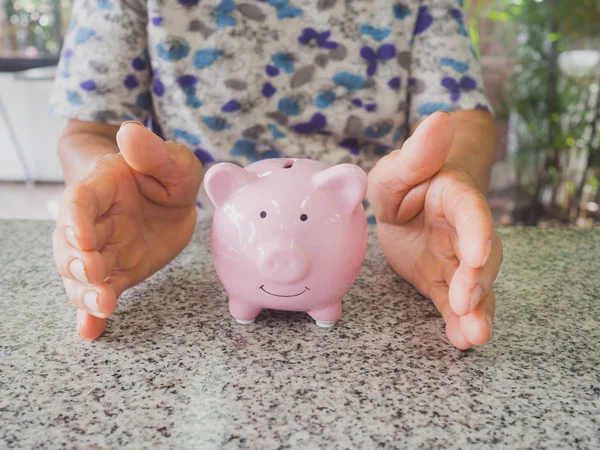 Old woman hand prevent Pink piggy bank standing on marble floor. Saving money for future plan and retirement fund concept