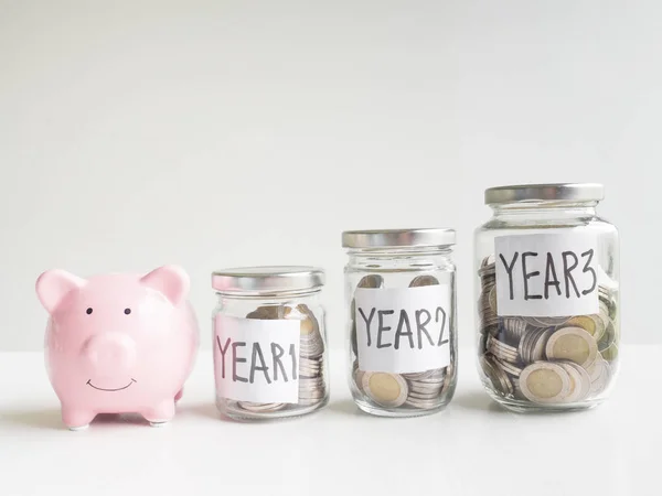 Banco piggy rosa com moedas em 3 garrafas de vidro, economizando dinheiro para o futuro plano e conceito de fundo de aposentadoria — Fotografia de Stock