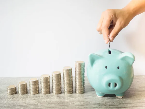 Woman hand putting coin into blue piggy bank with coins pile growth graph, saving money for future investment plan and retirement fund concept — Stock Photo, Image