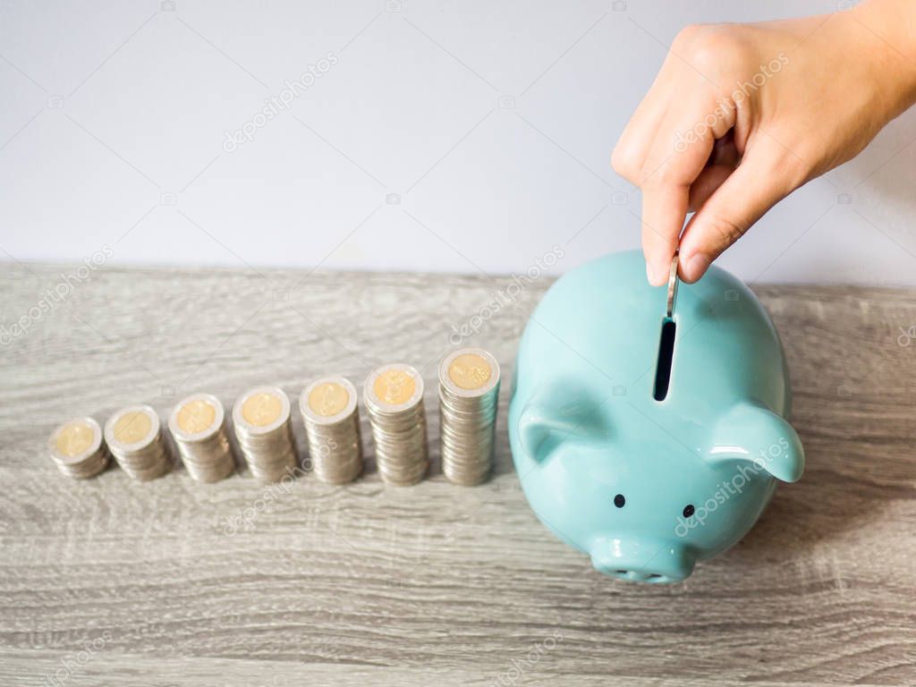 Woman hand putting coin into blue piggy bank with coins pile growth graph, saving money for future investment plan and retirement fund concept