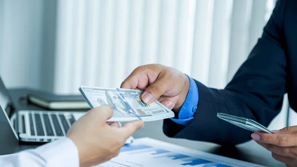 Takım elbiseli bir işadamının eli bir dolar tutuyor.