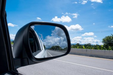 Yoldaki arabanın penceresinden güzel bulutlar ve gökyüzü manzarası, kırsal alanda seyahat ederken yan aynada yansıması..