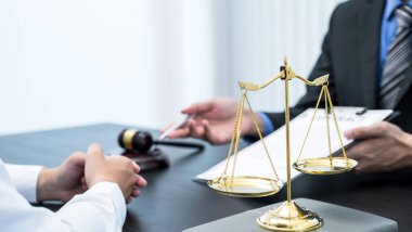 İş adamlarına iş anlaşmazlığı konusunda danışmanlık yapan erkek avukatın önünde duran adalet terazisi..