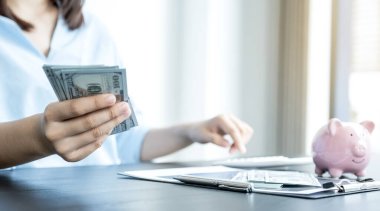 Kadının eli dolar banknotunu tutuyor ve masada bir domuz kumbarası var, başarılı olmak için işe başla, gelecek plan ve emeklilik fonu konsepti için para biriktir..