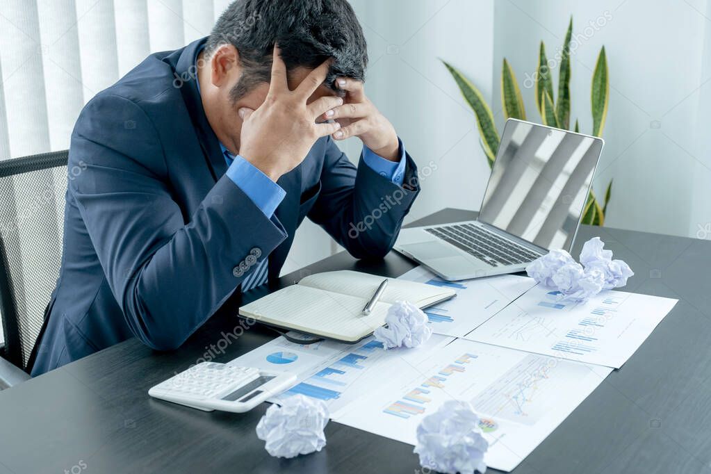 Businessman acted with tired stress anxiety from the frustrated business crisis, paperwork paper cube mess chaos on the table.