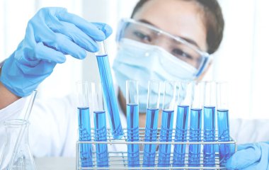 Bilim adamları laboratuarda araştırma ve analiz için mavi kimyasal sıvıyla dolu cam bir tüp tutuyorlar..