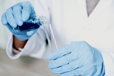 Bilim adamlarının elleri laboratuvarda araştırma ve analiz için mavi kimyasal sıvıyla dolu cam bir tüp tutuyor..