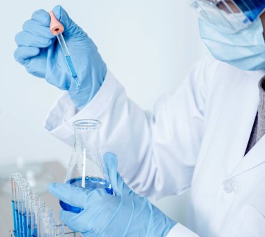 Bilim adamları pipeti tutuyor ve araştırma ve analiz için mavi kimyasal sıvıyı laboratuvara bırakıyorlar..