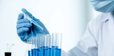 Bilim adamları pipeti tutuyor ve araştırma ve analiz için mavi kimyasal sıvıyı laboratuvara bırakıyorlar..