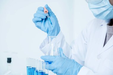 Bilim adamları pipeti tutuyorlar ve araştırma ve analiz için mavi kimyasal sıvıyı laboratuara bırakıyorlar..