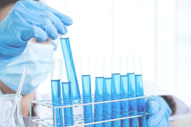 Bilim adamları laboratuarda araştırma ve analiz için mavi kimyasal sıvıyla dolu bir cam tüpü ellerinde tutuyorlar..