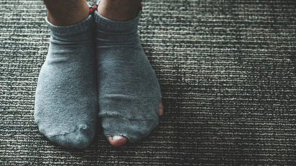 A pair of feet wearing old, dirty, and torn socks.