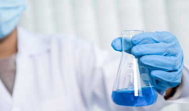 Bilim adamları laboratuarda araştırma ve analiz için mavi kimyasal sıvıyla dolu cam bir tüp tutuyorlar..