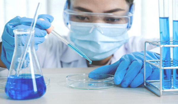 Scientists hold the pipette and drop the blue chemical liquid for research and analysis in a laboratory.