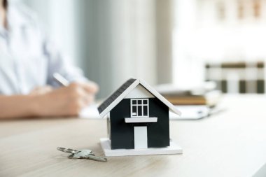 Bir emlakçının önünde duran ev modeli iş sözleşmesini, kirayı, satın almayı, ipoteği, krediyi ya da ev sigortasını alıcıya açıklar. .
