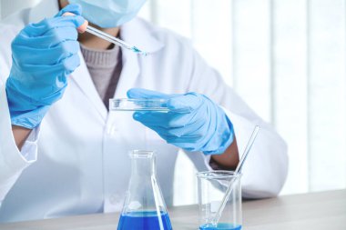 Bilim adamları pipeti tutuyor ve araştırma ve analiz için mavi kimyasal sıvıyı laboratuvara bırakıyorlar..