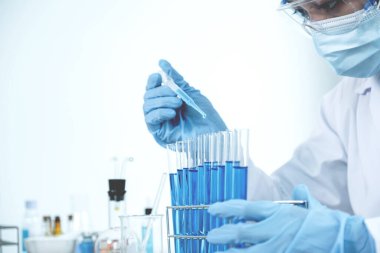 Bilim adamları pipeti tutuyor ve araştırma ve analiz için mavi kimyasal sıvıyı laboratuvara bırakıyorlar..