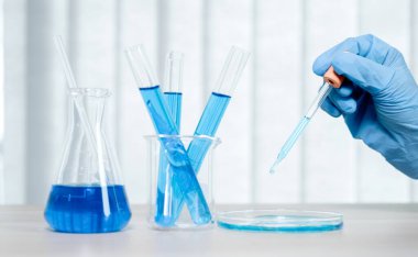 Bilim adamları pipeti tutuyor ve araştırma ve analiz için mavi kimyasal sıvıyı laboratuvara bırakıyorlar..