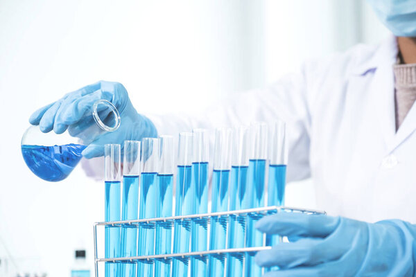 Scientists hold a glass filled with blue chemical liquid for research and analysis in a laboratory.