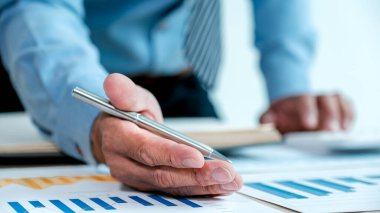 İşadamı, iş hedeflerini belirlemek ve yeni hedefe ulaşmayı planlamak için ofisteki bilgisayarı kullanarak grafiği analiz ediyor..