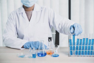 Bilim adamları laboratuarda araştırma ve analiz için mavi kimyasal sıvıyla dolu bir cam tüpü ellerinde tutuyorlar..