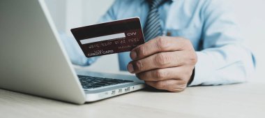 İş adamı elinde laptop, ödeme e-ticaret, internet bankacılığı ve gelecek tatiller için para harcayan evden online alışveriş için kredi kartı tutuyor..