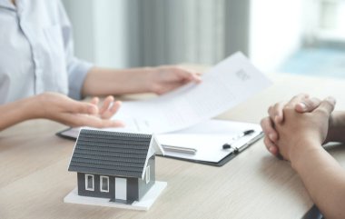 Bir emlakçının önünde duran ev modeli iş sözleşmesini, kirayı, satın almayı, ipoteği, krediyi ya da ev sigortasını alıcıya açıklar. .