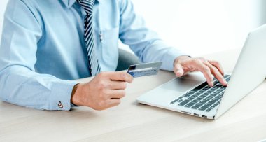 İş adamı elinde laptop, ödeme e-ticaret, internet bankacılığı ve gelecek tatiller için para harcayan evden online alışveriş için kredi kartı tutuyor..