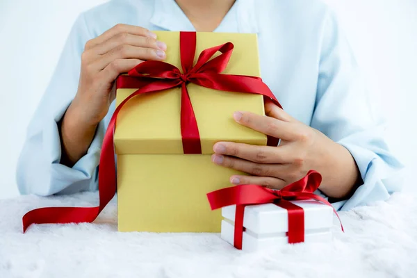 Woman hand in a blue shirt opening a gold gift box tied with a red ribbon present for the festival of giving special holidays like Christmas, Valentine\'s Day.