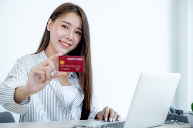 Kırmızı kredi kartı tutan uzun saçlı, güzel bir Asyalı kadının portresi. Gözleri kamerada pırıl pırıl parlıyordu. İndirimli ürünlere göre alışverişe hazır..