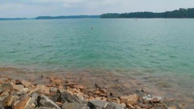 Küçük dalgalar güneşli bir günde puslu arka plan içinde ağaçların adaları ile yaz aylarında gölün kıyısında kayalar ve kayalar üzerinde çökmesini