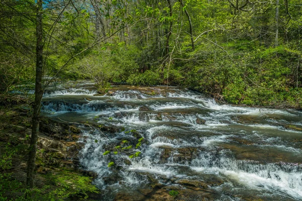初春の晴れた日には 滝から岩や岩まで白い水が流れる水のトレイルを速く歩く — ストック写真