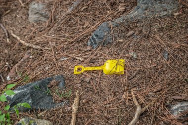Parlak sarı çocuk plaj küreği oyuncağı baş aşağı yere atıldı. Bir yaz günü, ormanlık alanda gölün kenarında.