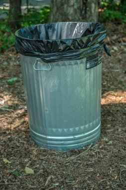 Açık bir teneke kutunun içine temiz bir torba yerleştirilmiş yepyeni metal çöp tenekesi. Yazın güneşli bir günde bir parkta.