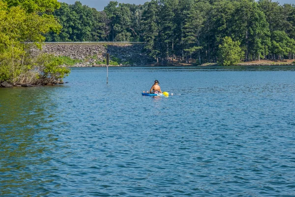 A young woman kayaking letting her dog go for a swim in the lake on a hot afternoon in summertime