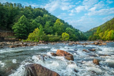Tennessee 'deki Ocoee nehrinde akan beyaz suyun yakın görüntüsü. Barajın arka planında dağlar ve sonbaharın başlarında bulutlu beyaz gökyüzü.