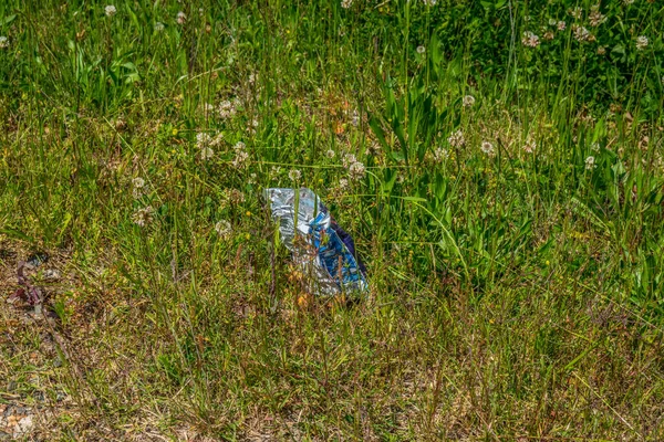 Boş cips torbası çimenlerin üzerine serilmiş güneşli bir günde dışarıdaki dikkatsizlik yüzünden çevreyi kirletiyor.