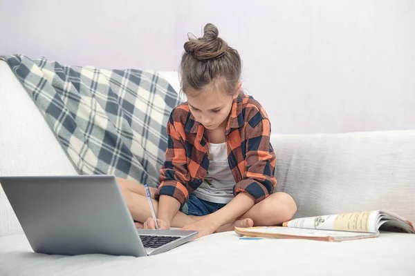 Enfant assis sur le canapé à la maison et fait des leçons en ligne — Photo