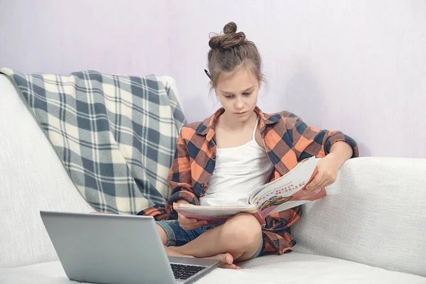 Kind sitzt zu Hause auf dem Sofa und liest ein Lehrbuch — Stockfoto