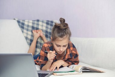 Evdeki kanepede oturan bir çocuk dikkatle okul kitabı okuyor.