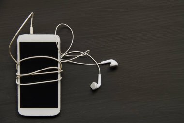 Kulaklıklarla ahşap arka plan üzerinde beyaz cep telefonu