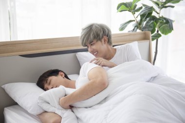 Asyalı eşcinsel erkekler yatakta yatıp erkek arkadaşlarıyla LGBT çiftleri konseptiyle dalga geçiyorlar..