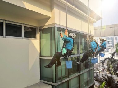 Rope erişim temizlik çalışanı giyen emniyet kemeri sert şapka çalışan halat üzerinde azalan yükseklikte çalışma bir hastane kompleksi cam duvar yıkıyor. 