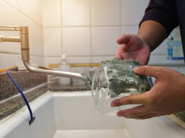 Bulaşık yıkama. Erkek eller yıkama köpük ve sofra dolu mutfak lavabo karşı Yeşil temizlik sünger ile cam kase