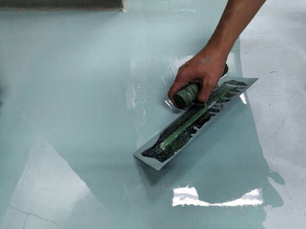 Construction workers are painting the floor using the method self-leveling epoxy.spreading self leveling compound with trowel.Self-leveling epoxy. Leveling with a mixture of cement floors.